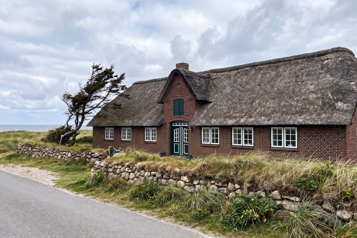 Foto eines Friesenhauses mit Reetdach und rotem Klinker an einer Straße am Meer